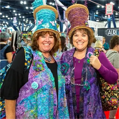 » Country Heritage Tours » Country Heritage Tours Two smiling women wearing thread spool hats at a quilting convention