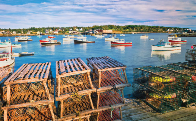 » Country Heritage Tours Lobster traps sitting on a dock in Maine with boats in the harbor behind it
