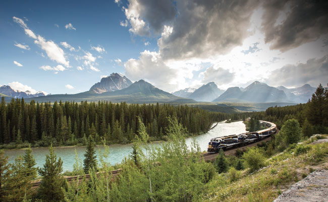 » Country Heritage Tours Rocky Mountaineer train passing beside a winding river with mountains in the background