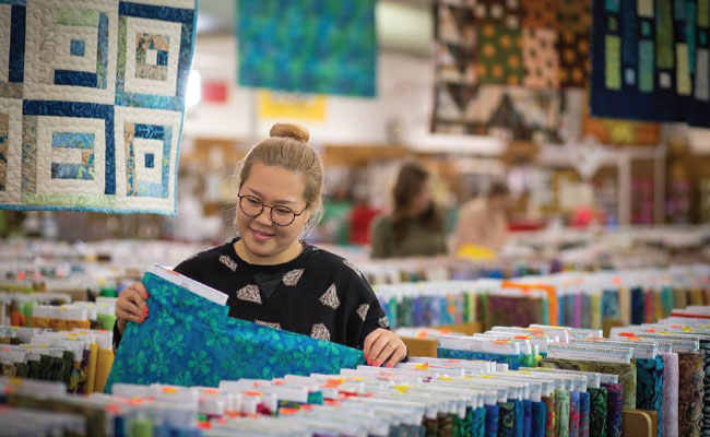 » Country Heritage Tours Woman smiling looking at yards of fabric in a quilt store