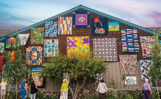 » Country Heritage Tours Side of barn building with quilts hung on it and women in the foreground looking at the barn
