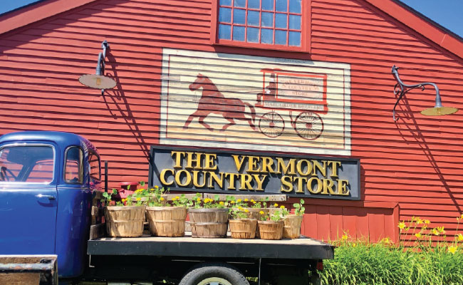 » Country Heritage Tours Vermont country store exterior shot red barn with antique truck and planter pots on its bed