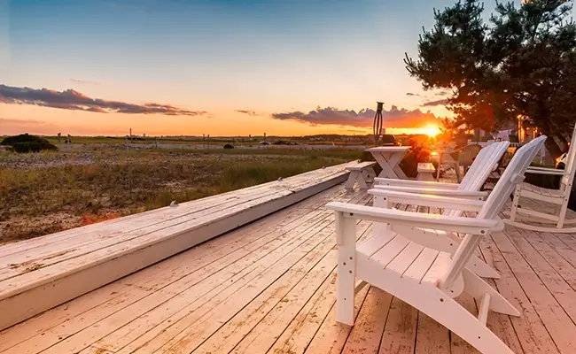 » Country Heritage Tours White Adirondack chairs on a wooden deck at Sunset looking at the sand dunes